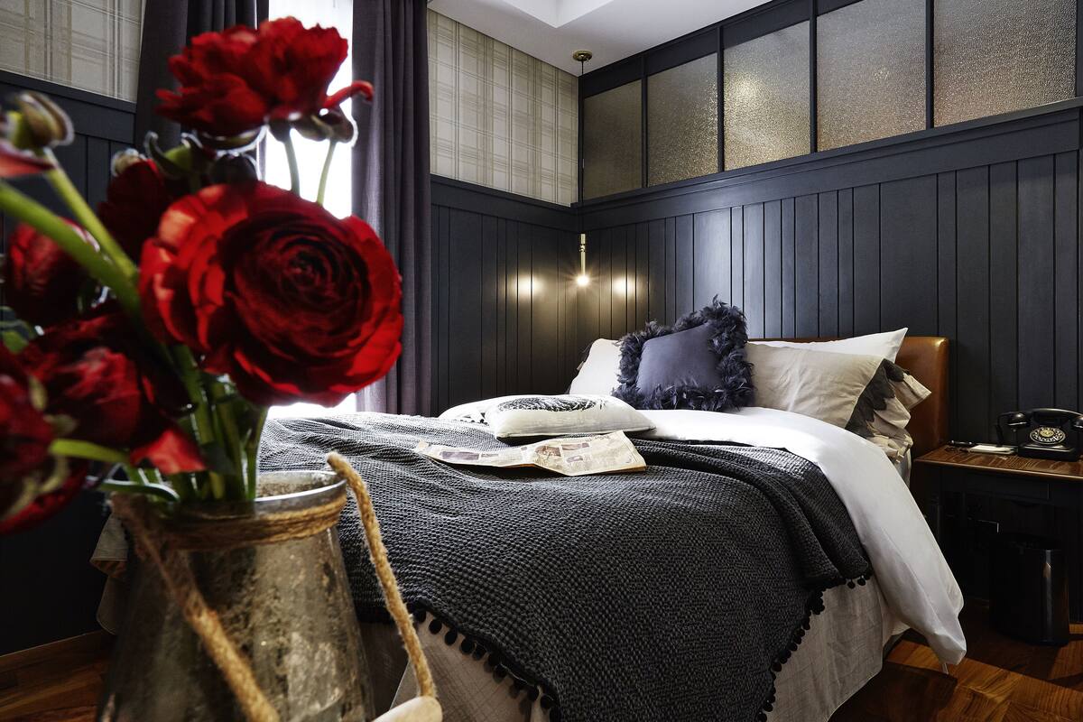 A bedroom with a bed, a nightstand, a vase with red roses, and a wall with a textured panel.