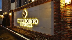 A hotel sign with the name "HOTEL ROSETO BOUTIQUE HOTEL" illuminated against a brick wall. - Pocheon Hotel Roseto (Pocheon)