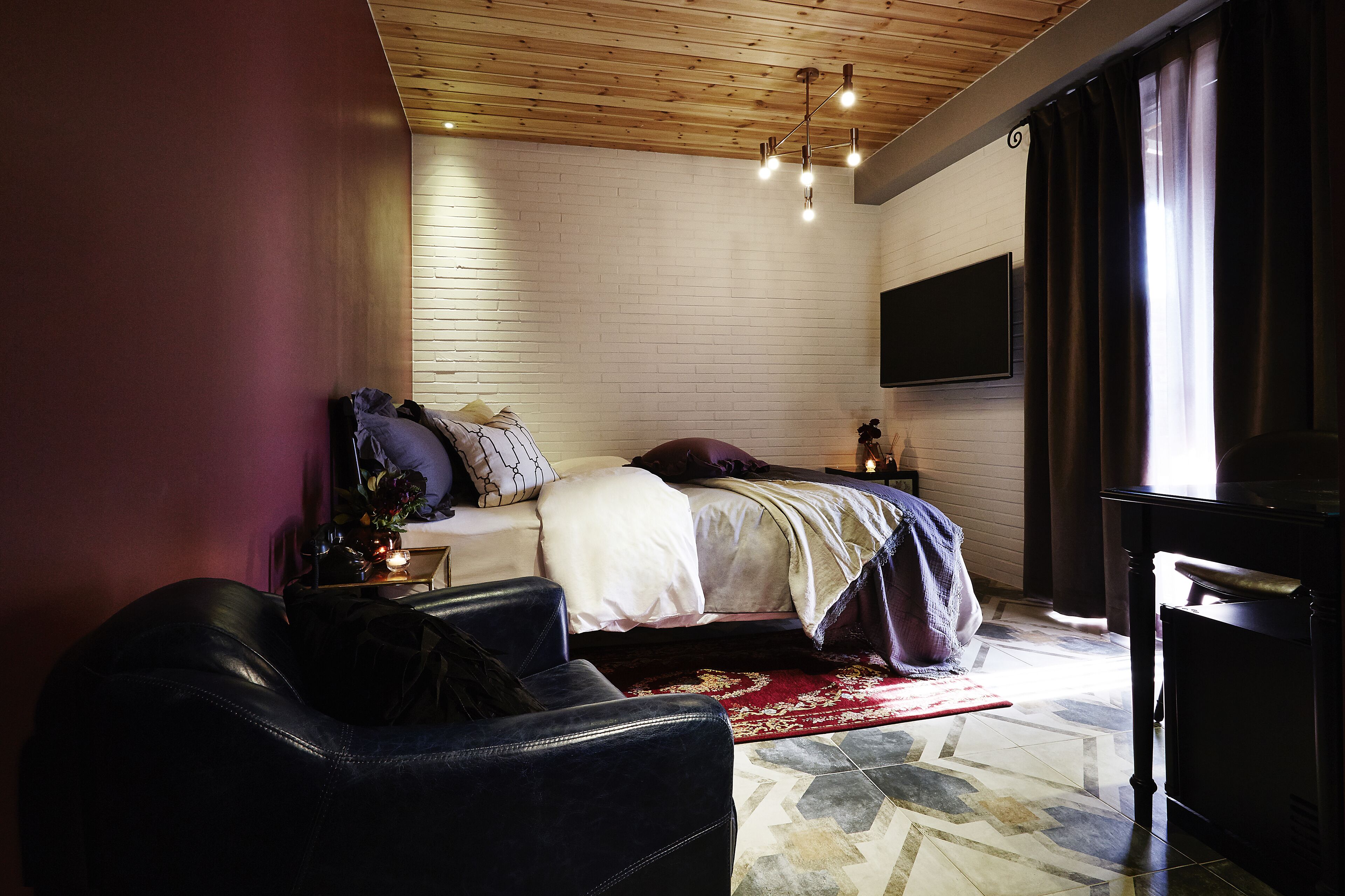 Ein Schlafzimmer mit einem Bett, einem an der Wand montierten Fernseher, einem Ledersessel und einer Holzbalkendecke.
