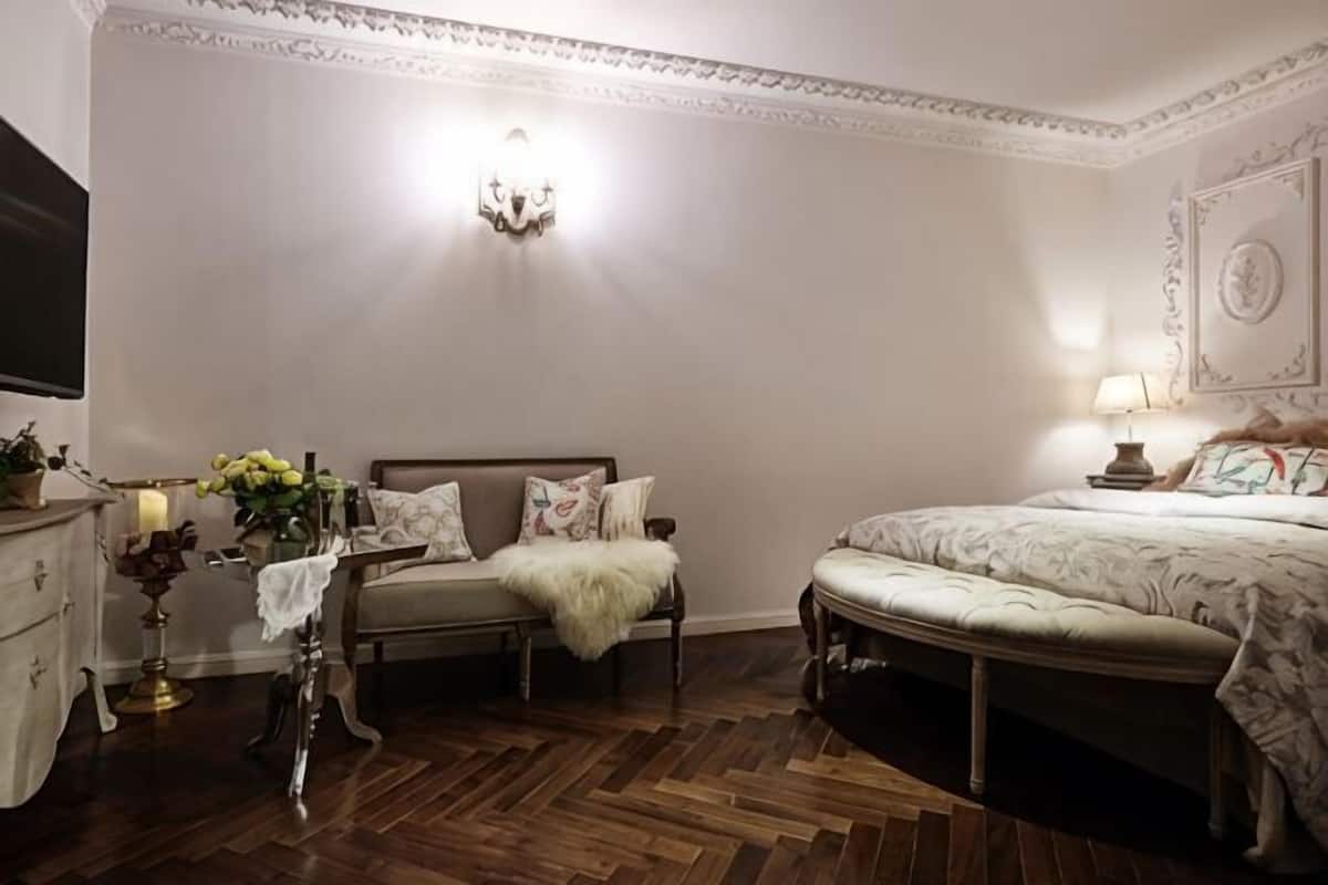 A bedroom with a bed, a bench, a dresser, and a wall-mounted light fixture.