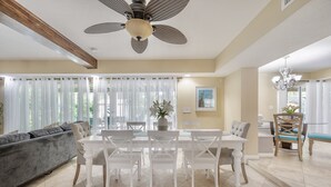 A modern dining area with a white table and chairs, a ceiling fan, and a view of the outdoors through large windows. - ✨River Front✨Heated Pool Estate-Large Group,Busch Garden,USF, Sleeps 14 (Tampa)