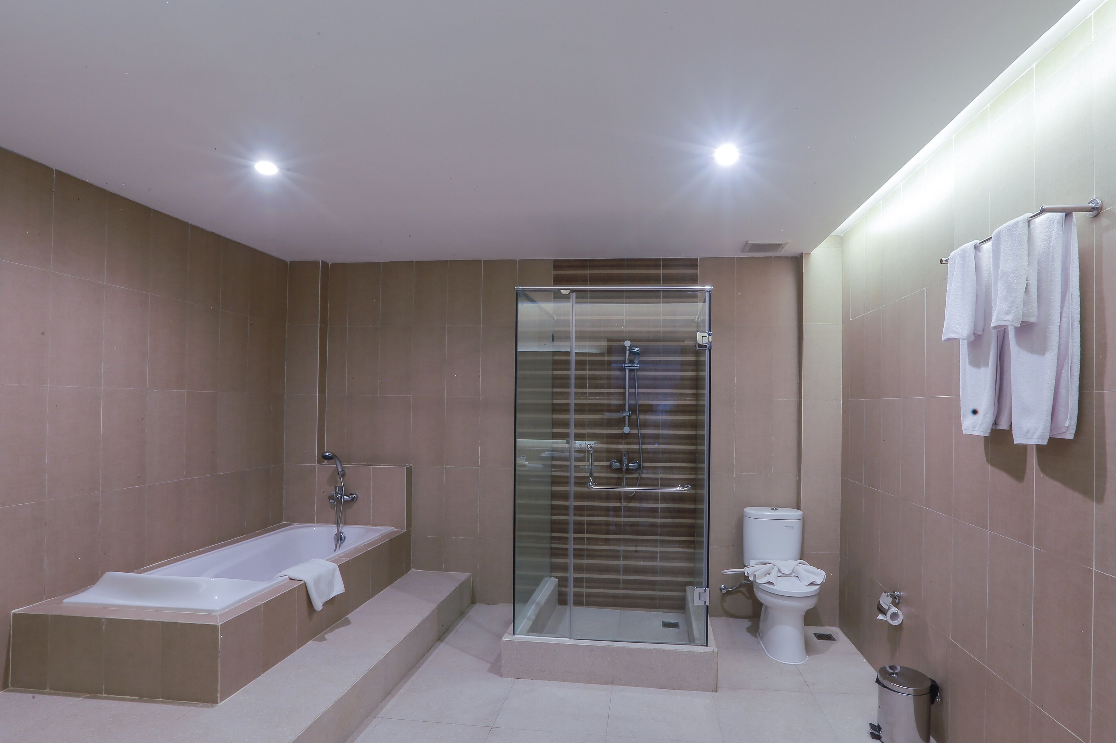 A modern bathroom with a bathtub, glass-enclosed shower, toilet, and a trash bin.