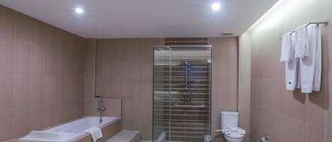 A modern bathroom with a bathtub, glass-enclosed shower, toilet, and a trash bin.