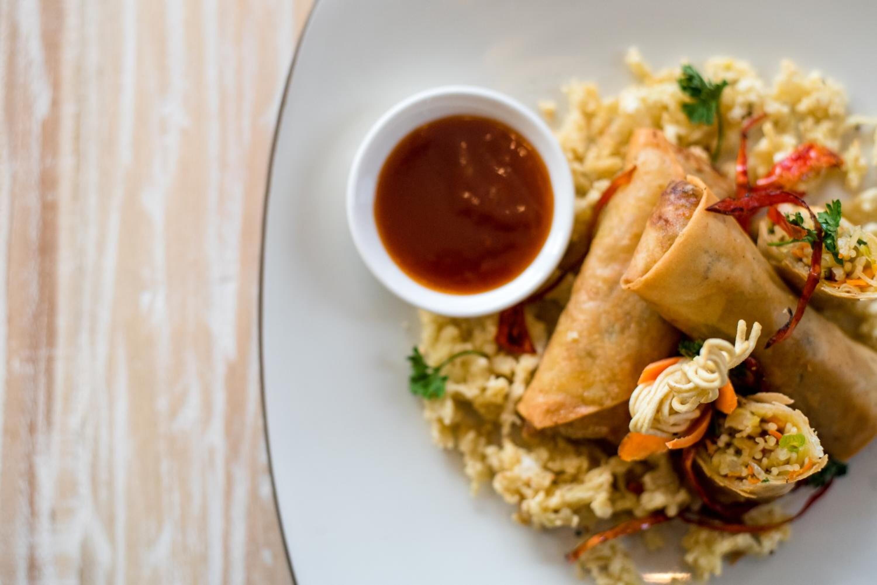 A plate of spring rolls with a side of dipping sauce and a decorative garnish.