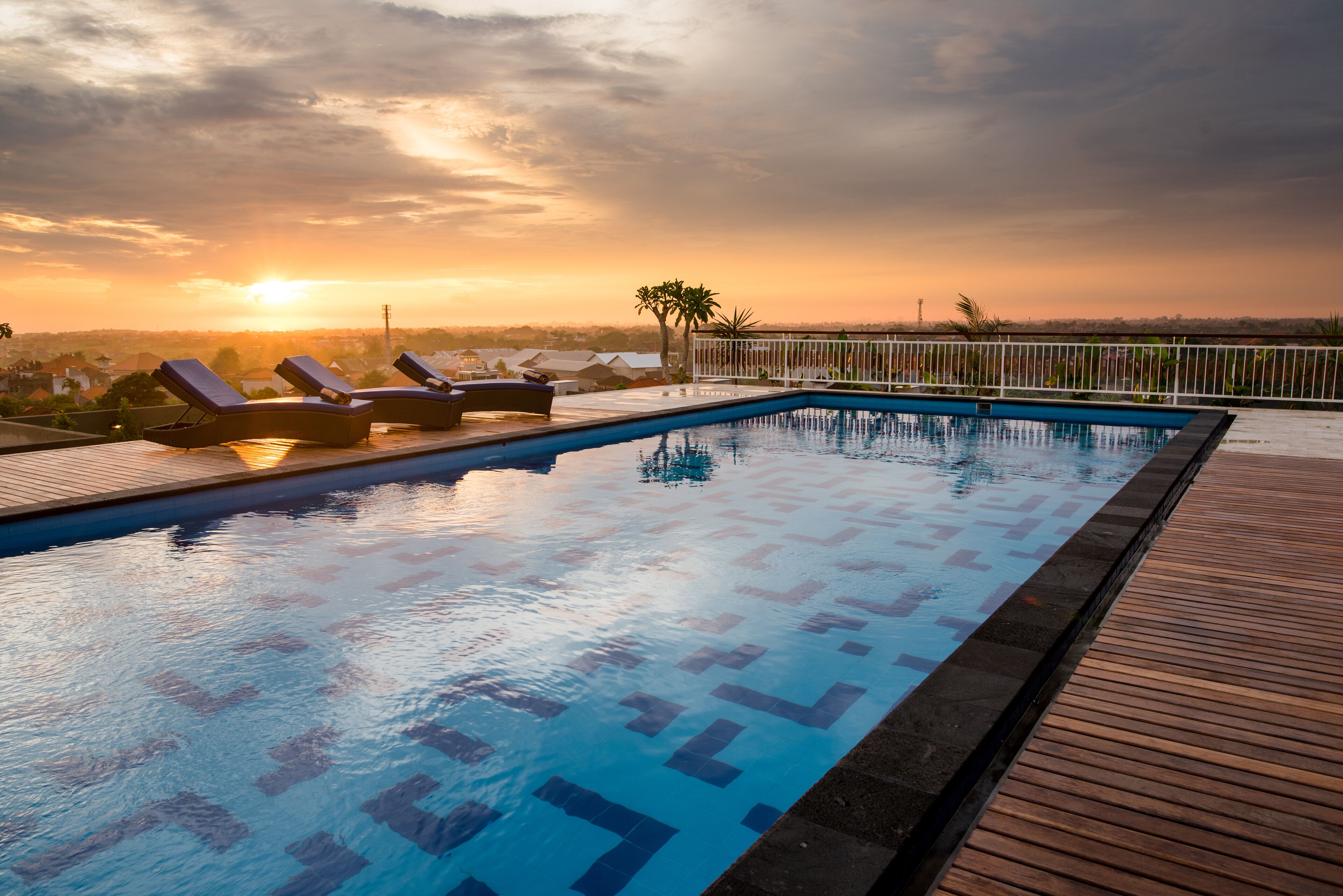 Une piscine dotée de chaises longues et d’une terrasse en bois, le tout entouré d’une clôture.