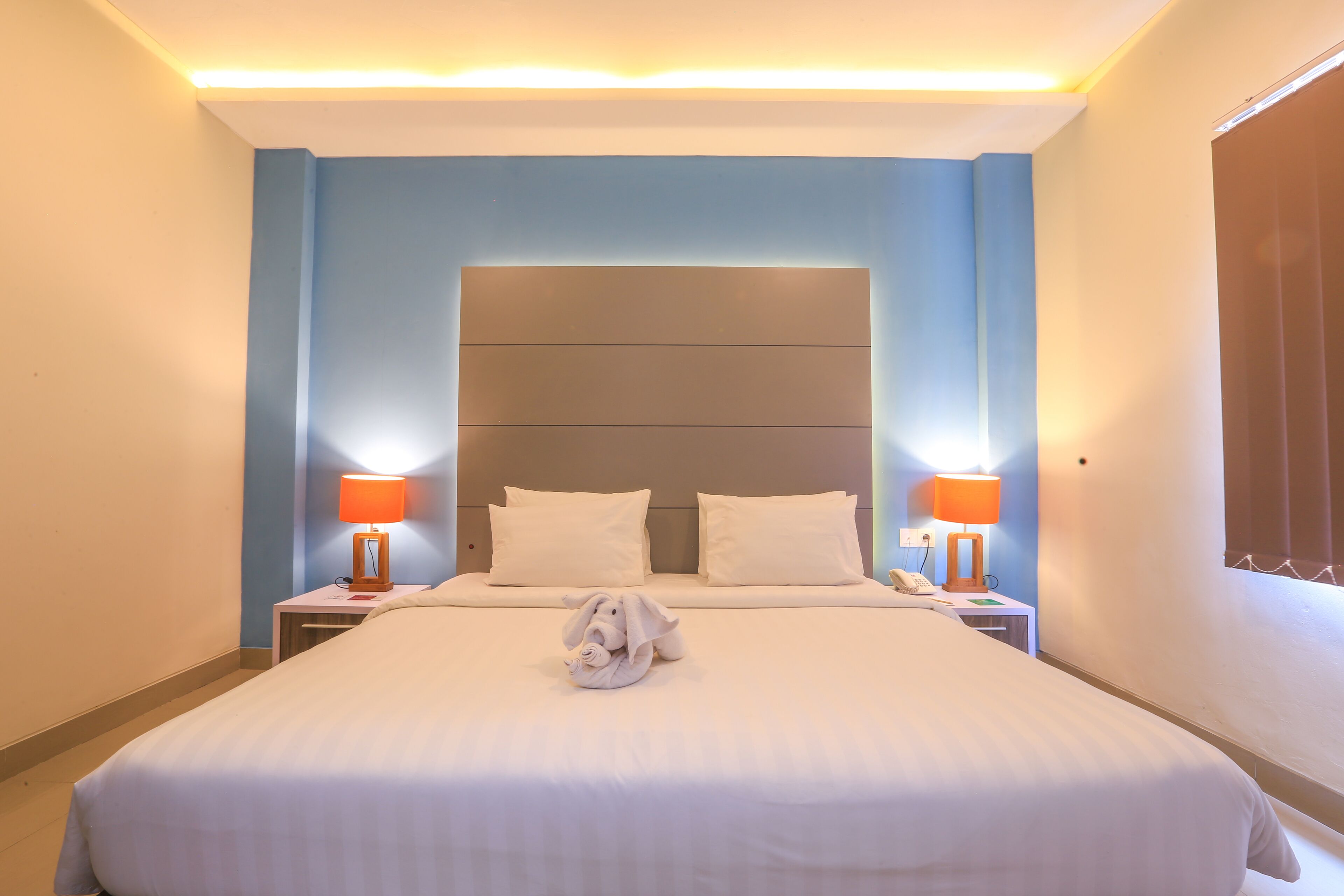 Een hotelkamer met een groot bed, twee bedlampen, een hoofdeinde en een raam met gordijnen.