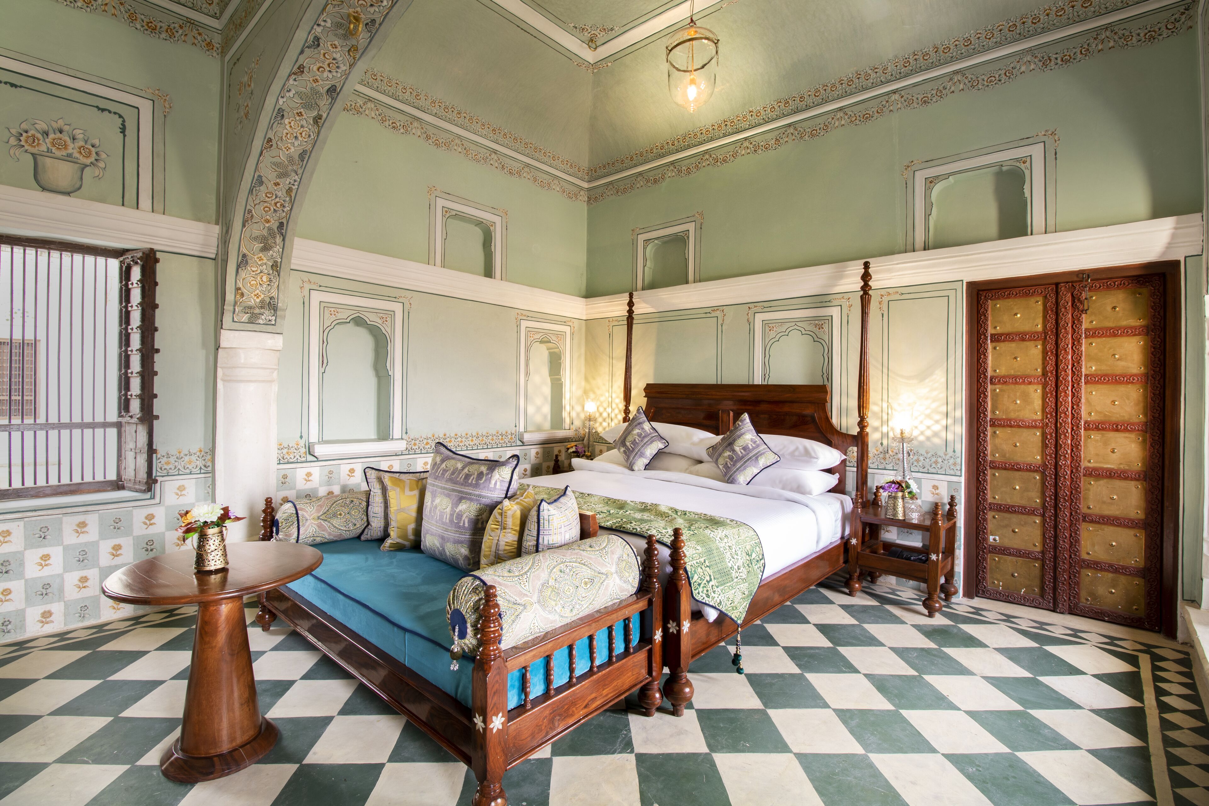 A traditional bedroom with a four-poster bed, a small round table, and a checkered floor.