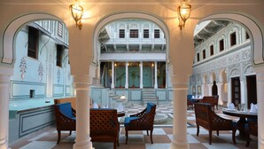 A covered dining area with checkered flooring, wooden chairs with blue cushions, and a view of a building with ornate architecture through an archway. - The Legacy Mandawa (Jhunjhunu)