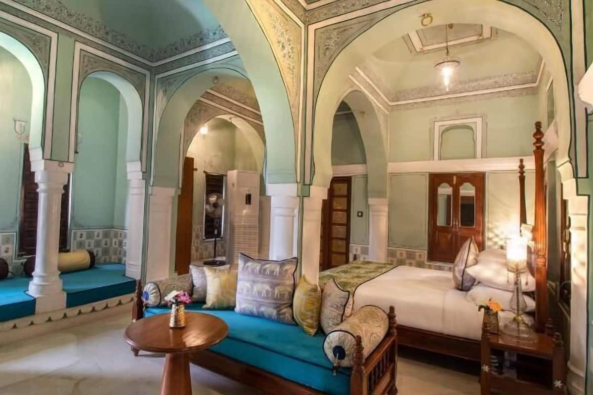 A room with a bed, a sofa, a table, and a chair. There are arched doorways and a chandelier.