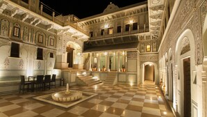 A grand, ornate hotel courtyard with a checkered floor, a central fountain, and a bar area. - The Legacy Mandawa (Jhunjhunu)