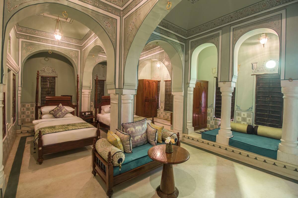 A luxurious bedroom with a large bed, a sofa, and a small table. There are multiple arches and columns in the room.