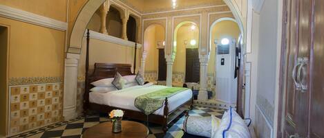 A hotel room with a four-poster bed, a checkered floor, and ornate ceiling arches.