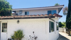 A single-story house with a tiled roof, a white exterior, and a small porch area with potted plants.