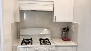 A compact kitchen with a gas stove, oven, and white cabinets.