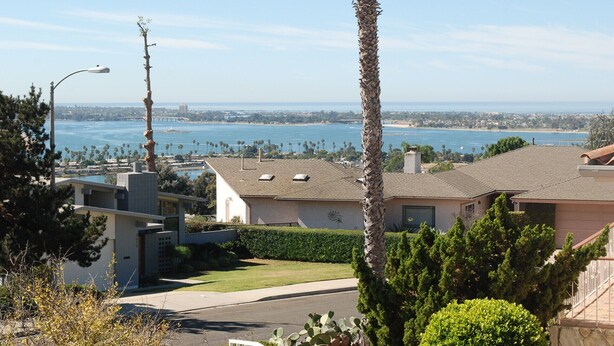A residential area with houses, a clear view of the ocean, and a bridge in the distance.