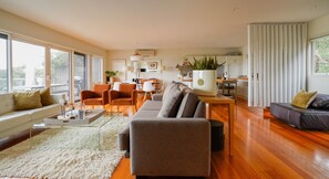 A spacious living room with a sofa, chairs, a coffee table, and a dining area. - Salt Bush - Great views nestled  in the moonahs (St Andrews Beach)