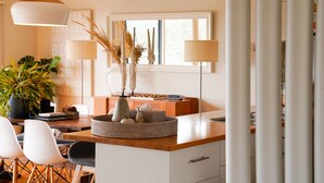 A modern kitchen with a wooden countertop, white chairs, a large potted plant, and a window with a view. - Salt Bush - Great views nestled  in the moonahs (St Andrews Beach)