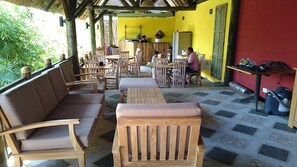 Uma área de estar coberta ao ar livre, com móveis de madeira, uma mesa de jantar e cadeiras.