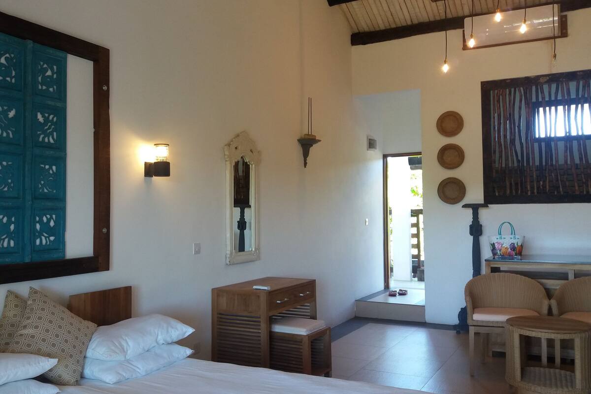 A bedroom with a bed, bedside tables, a mirror, and a view of the outside.