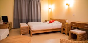 Quarto bem arrumado com cama de madeira, mesas de cabeceira, um banco e uma escrivaninha.