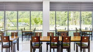 A dining area with tables and chairs, large windows with a view of greenery and a building outside. - Geumgangsong Ecorium (Uljin)