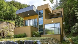 A modern two-story house with large windows and a balcony, surrounded by a natural landscape. - Geumgangsong Ecorium (Uljin)