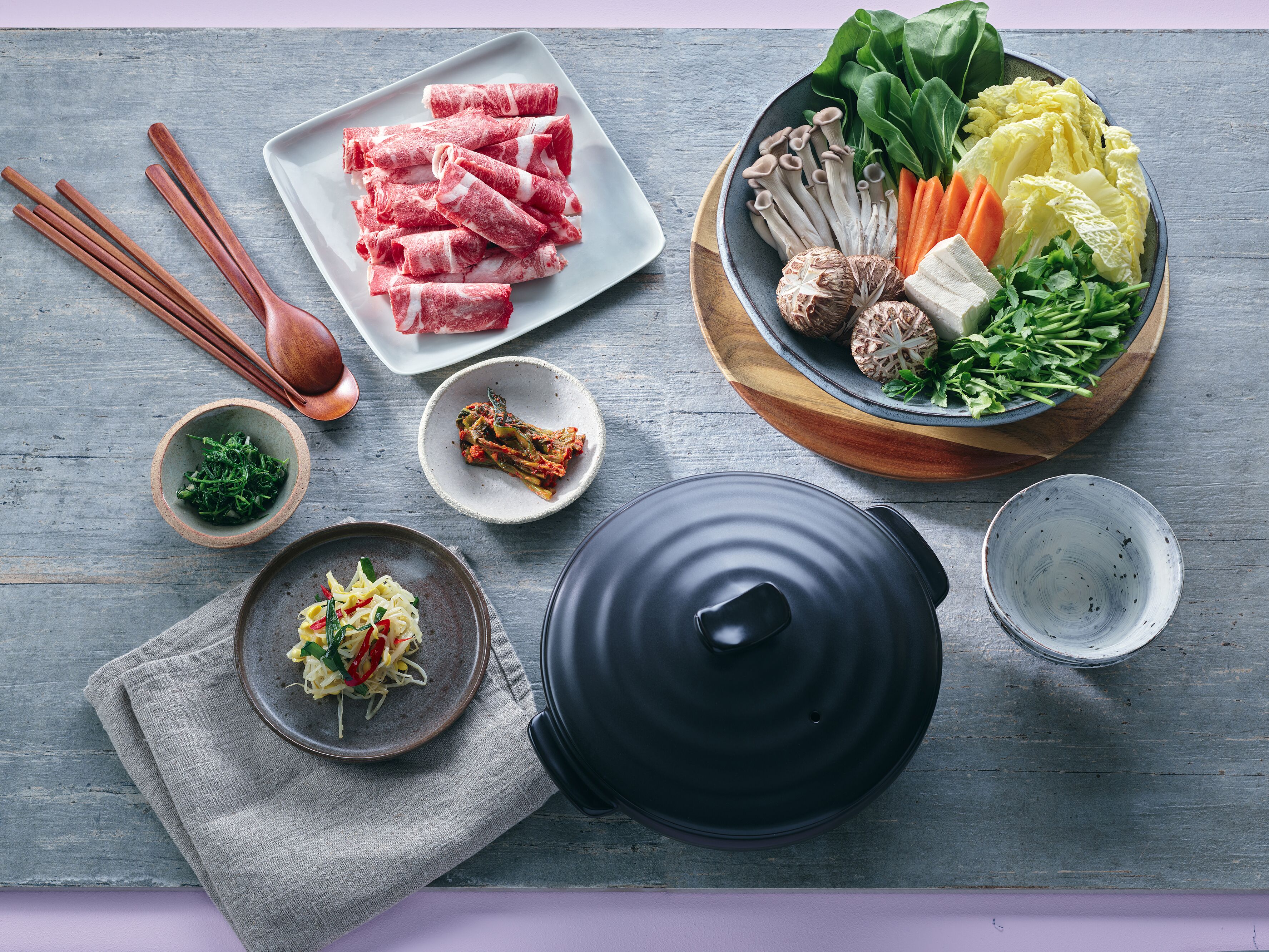 A table with various food items, including meat, vegetables, and a pot.