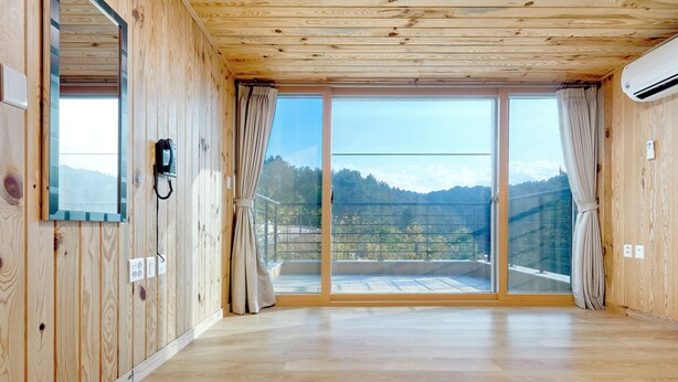 A room with wooden walls, a large sliding glass door to a balcony, and a telephone mounted on the wall. - Geumgangsong Ecorium (Uljin)