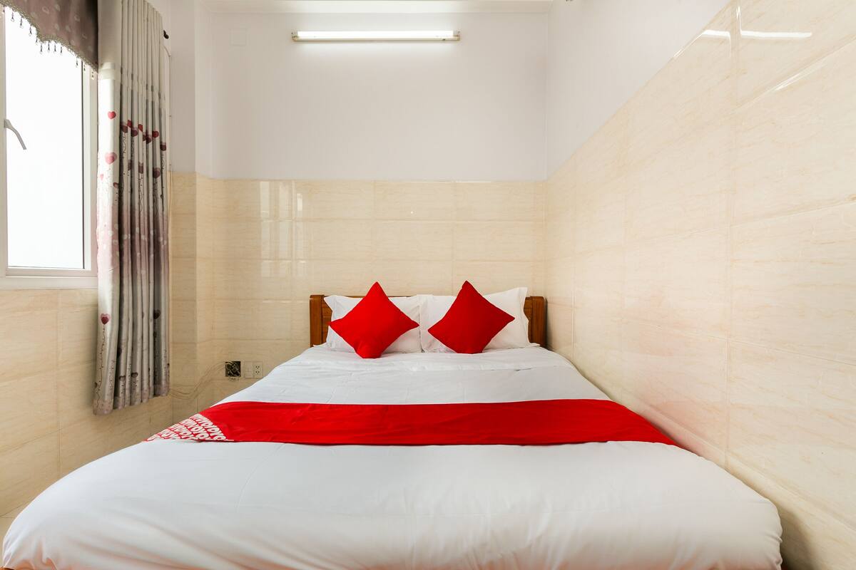 Een opgemaakt bed met wit en rood beddengoed, een houten hoofdbord en een rode plaid.