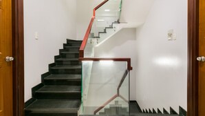 Un escalier avec des rampes en verre et des mains courantes en bois, menant à l’étage supérieur.