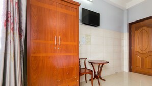 Une pièce comprenant une armoire en bois, un téléviseur à écran plat fixé au mur, une petite table ronde avec deux chaises et une porte ornée d’un panneau décoratif.