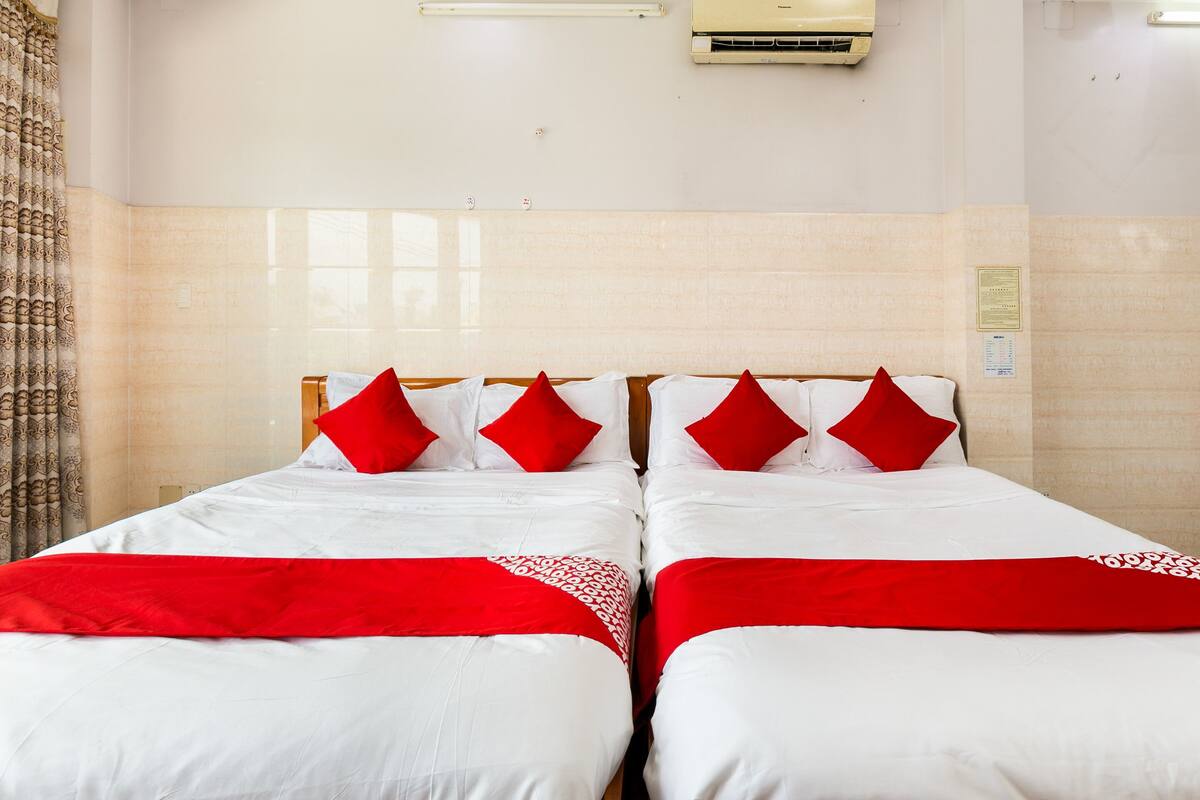 Een hotelkamer met twee bedden, elk voorzien van witte beddengoed en rode accenten, een betegelde muur en een airconditioning.