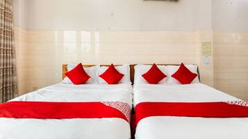 A hotel room with two beds, each with white bedding and red accents, a tiled wall, and an air conditioning unit.