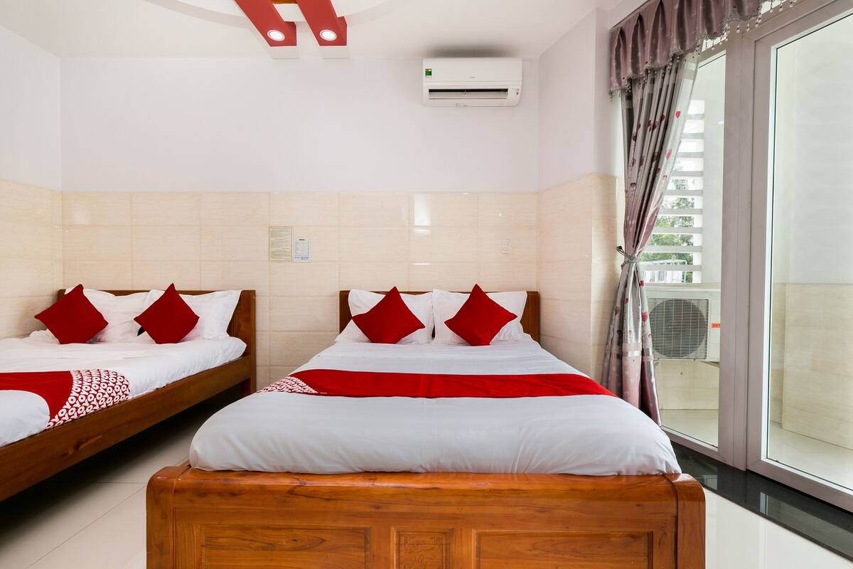 Een hotelkamer met twee bedden, elk met rode en witte beddengoed, een houten hoofdeinde en een groot raam met gordijnen.