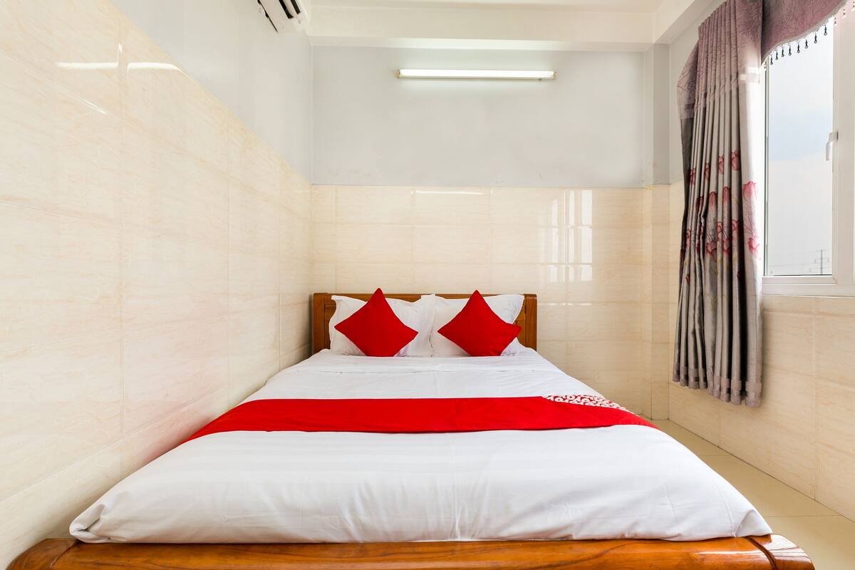 Een net opgemaakt bed met een houten hoofdbord, wit beddengoed en rode accenten.
