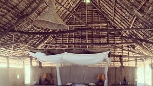 Una habitación rústica con techo de paja, una cama con dosel y una mesita de noche con lámpara.