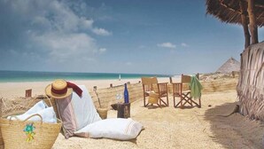 Escena de playa con una cabaña de paja, una silla de playa, un sillón reclinable y una cesta de mimbre.