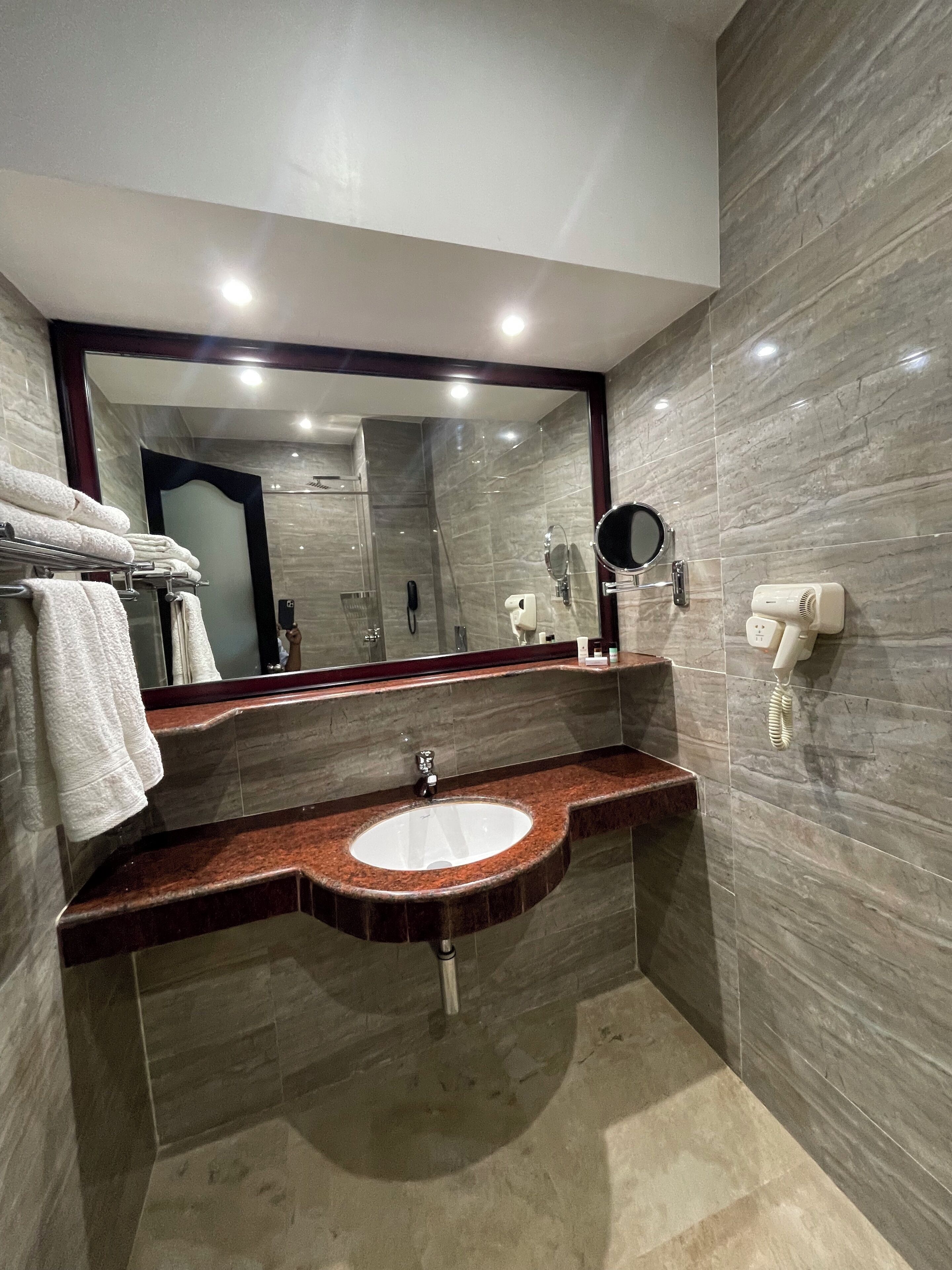 A modern bathroom with a marble vanity, a large mirror, a glass shower enclosure, and a towel rack with neatly folded towels.