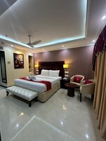 A modern hotel room with a large bed, a sitting area with a table and chairs, and a ceiling fan.