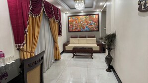 A dining area with a table set for four, a sofa, and a chandelier. - Sajjoys Hotel (Varkala)