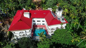 A large, multi-story building with a red roof, surrounded by lush greenery. - Sajjoys Hotel (Varkala)