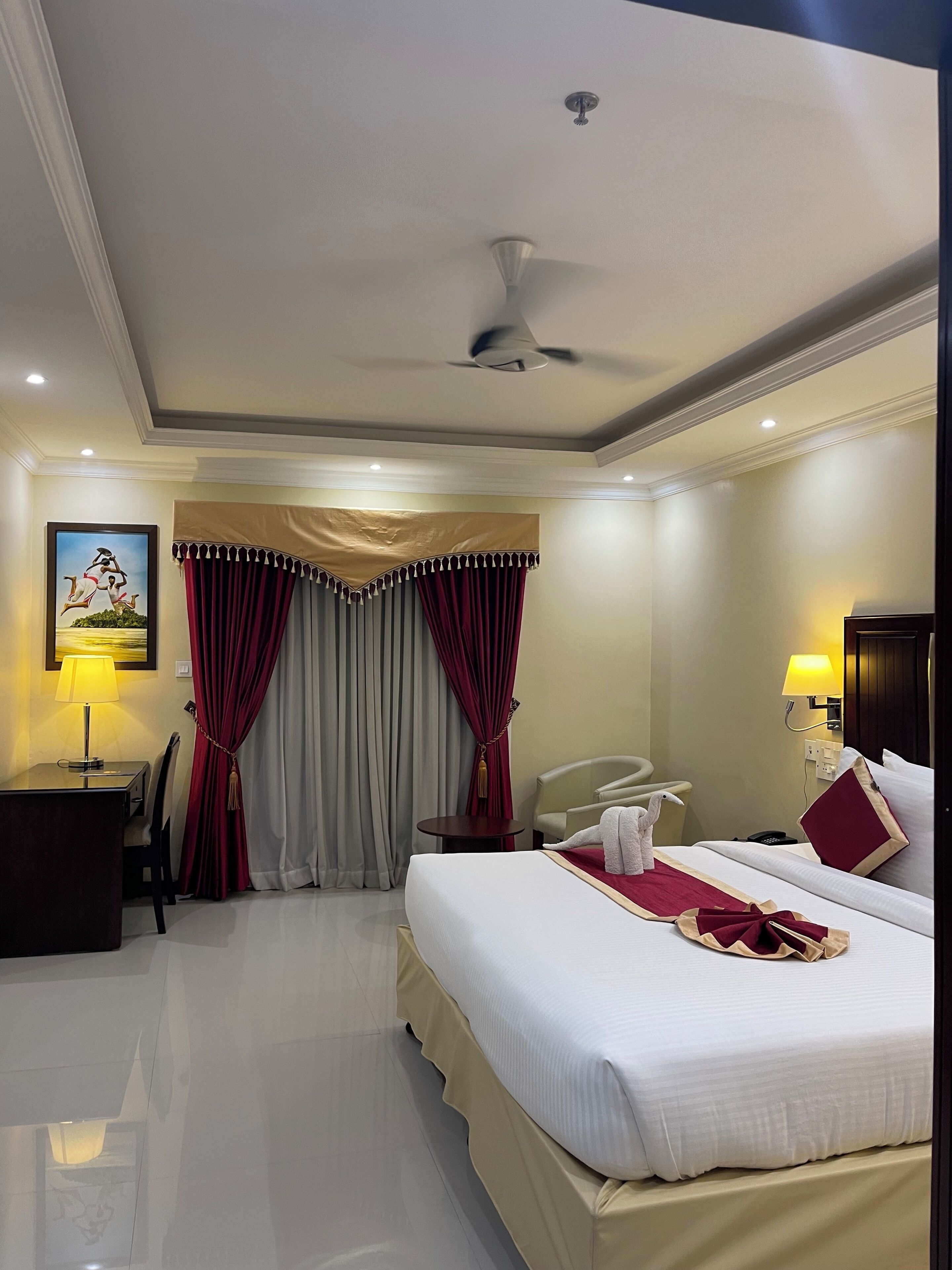 A hotel room with a bed, a desk, a chair, a lamp, and a ceiling fan.