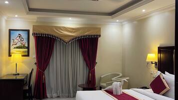 A hotel room with a bed, a desk, a chair, a lamp, and a ceiling fan.