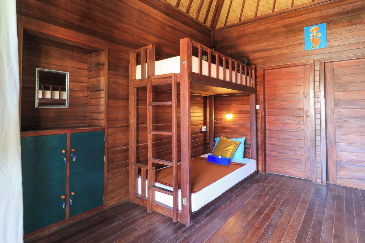 Une pièce de cabane en bois avec des lits superposés, une armoire verte et un tableau encadré au mur.