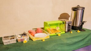 Une table mise pour le petit-déjeuner, avec une nappe verte, une machine à café, un grille-pain et divers éléments pour le petit-déjeuner, comme des couverts et des assiettes.