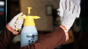 Une personne tenant un flacon pulvérisateur étiqueté « Haston » et un chiffon.
