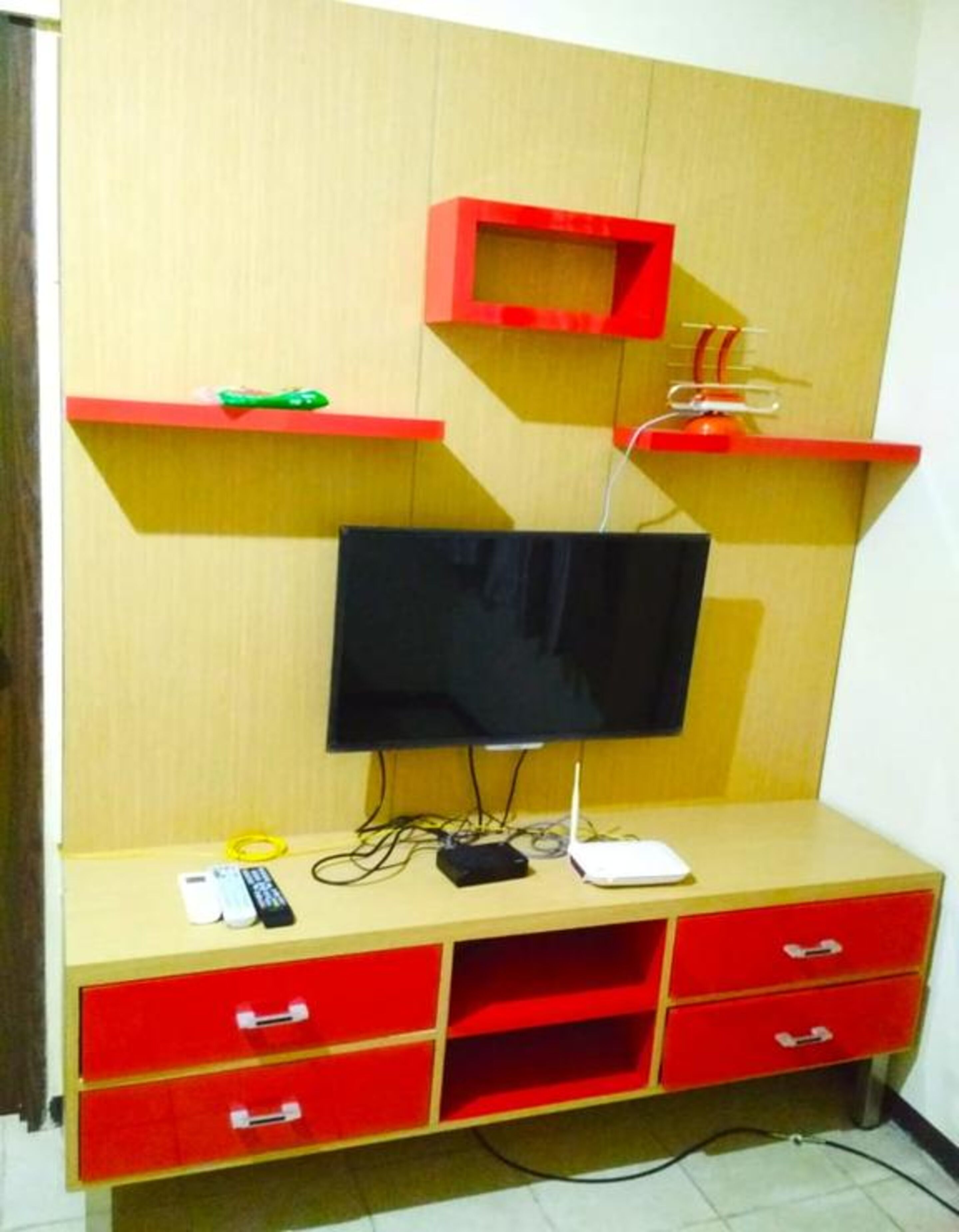 Un mobile contenitore in legno con TV a schermo piatto, cassetti rossi e ripiani.