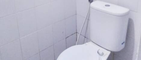 Un baño pequeño con azulejos blancos, un inodoro y una zona de ducha.