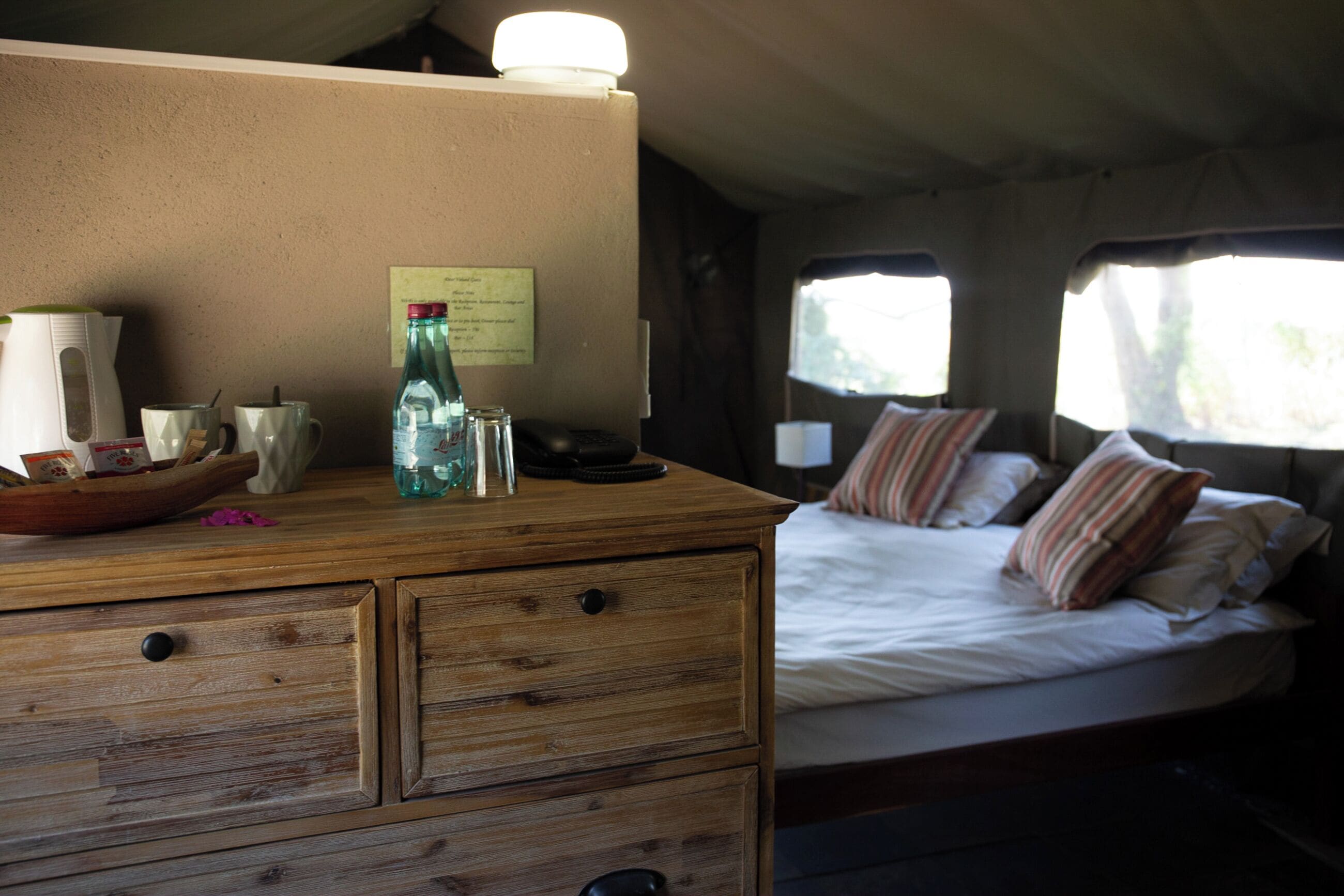 A bedroom with a wooden dresser, a bed with striped pillows, and a window with curtains.