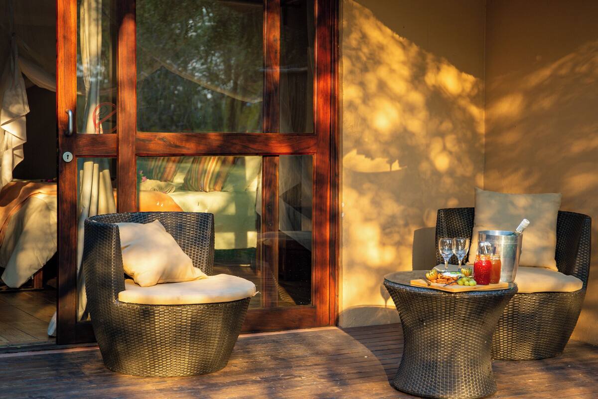 A sunlit outdoor seating area with wicker chairs and a table set with snacks and drinks.